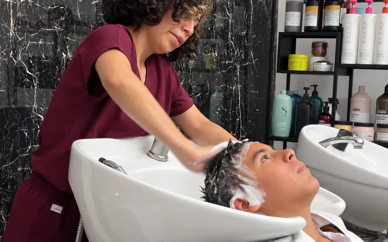 Estilista del equipo lavando el cabello de un cliente en el área de lavado
