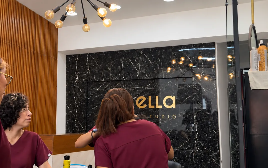 Equipo de Él & Ella con uniforme vino frente a la recepción de mármol negro con el logo dorado