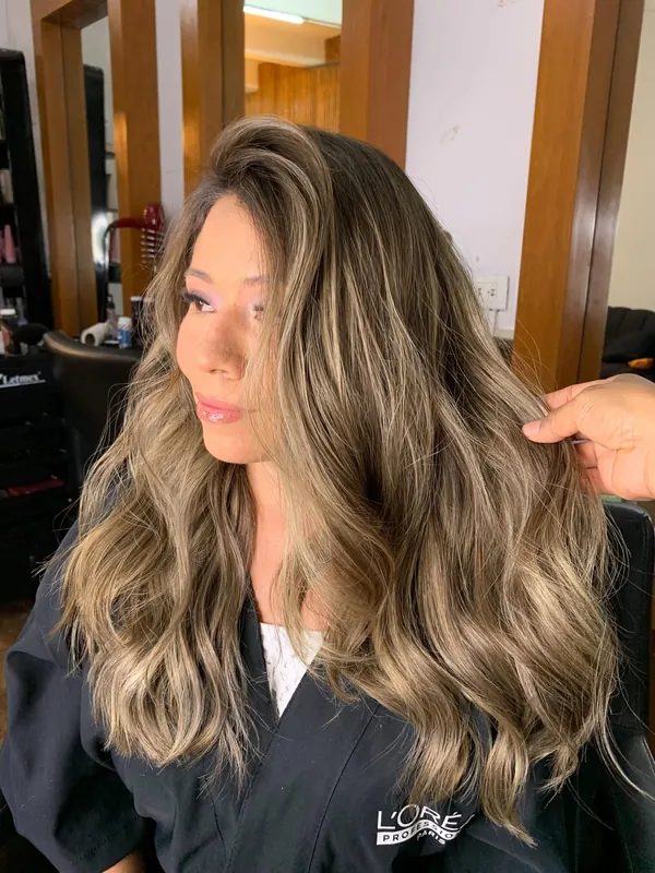 Clienta de perfil con mechas rubio cenizo y ondas suaves sobre capa del salón